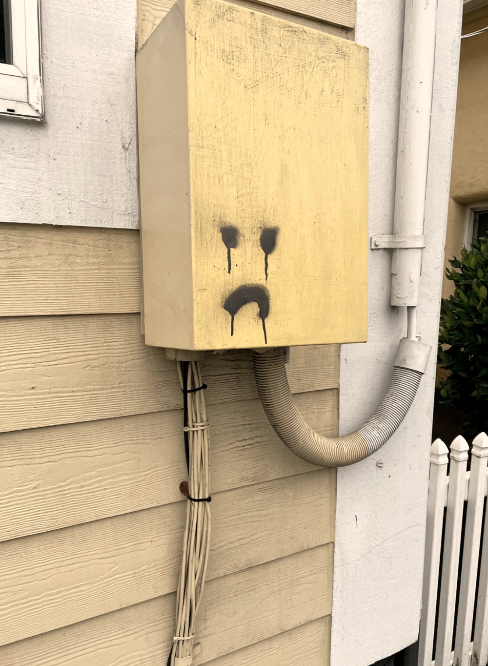 A sad face spray painted on the side of a yellow building. The paint dripped, so it looks like it's crying.