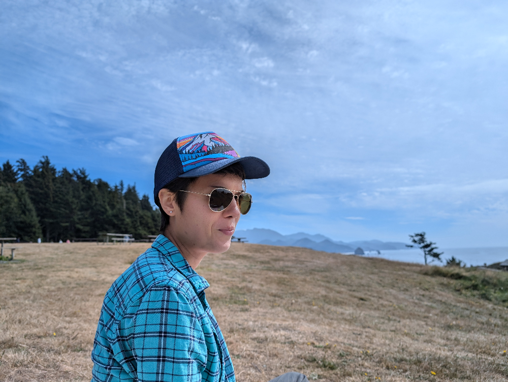 Radiance glancing over their shoulder at the beach, smiling slightly as they see their photo is being taken.