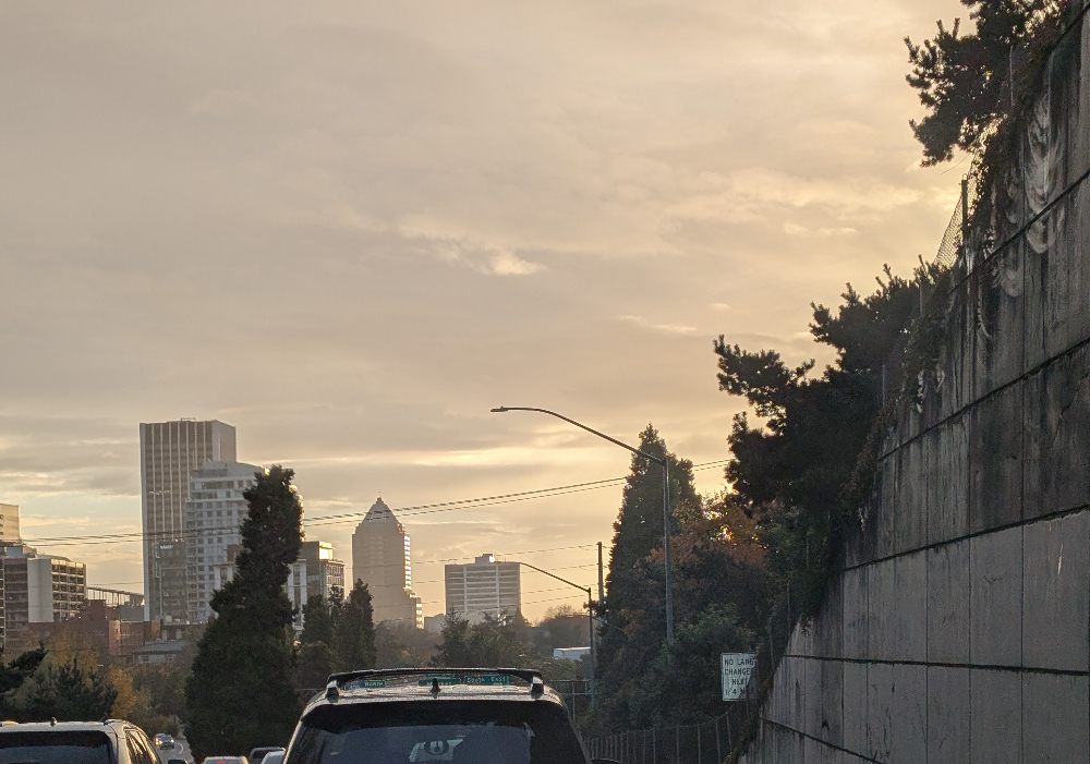 Sunrise over the city, with tall buildings illuminated from behind by the sun, the sky lit with golden light.