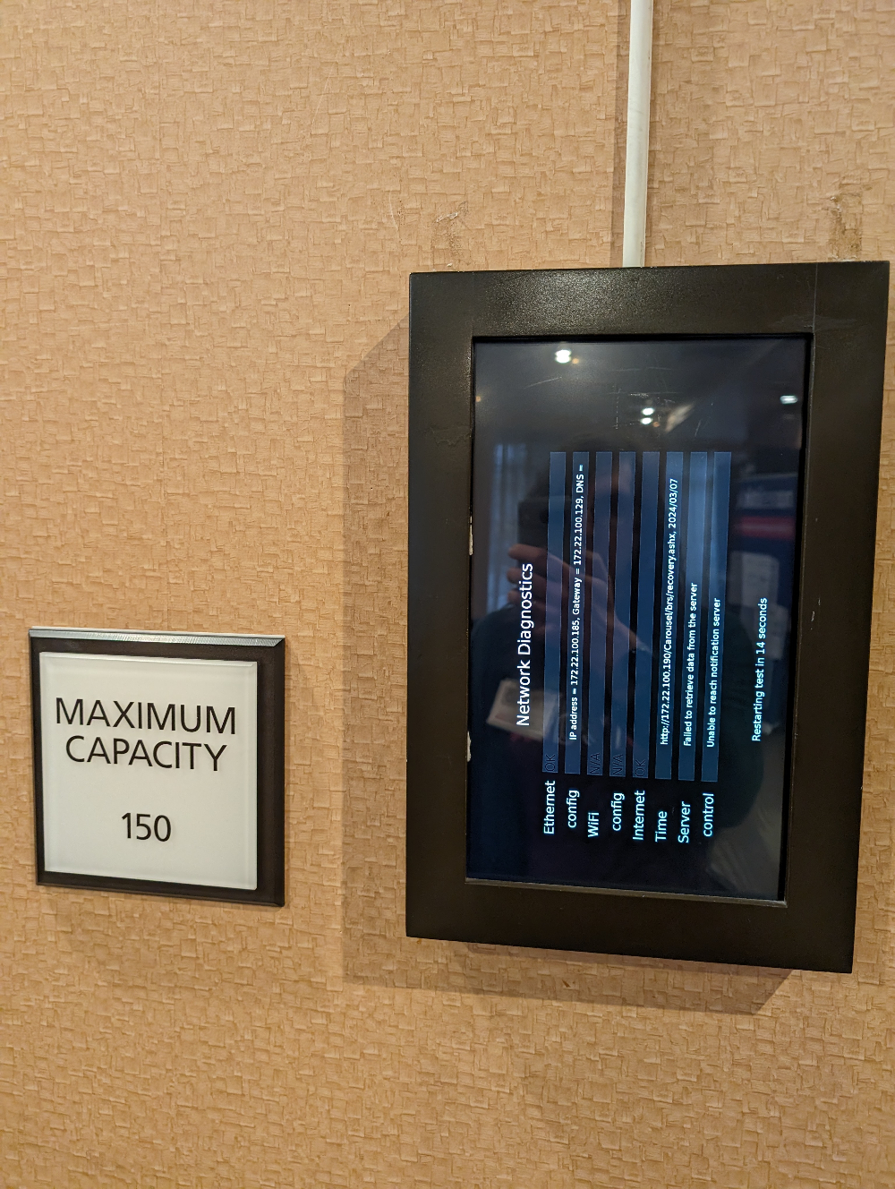 Monitor at the entrance to a hotel ballroom, but rather than showing who is scheduled for the meeting it has a network configuration screen that is displayed sideways. Maximum capacity 150.